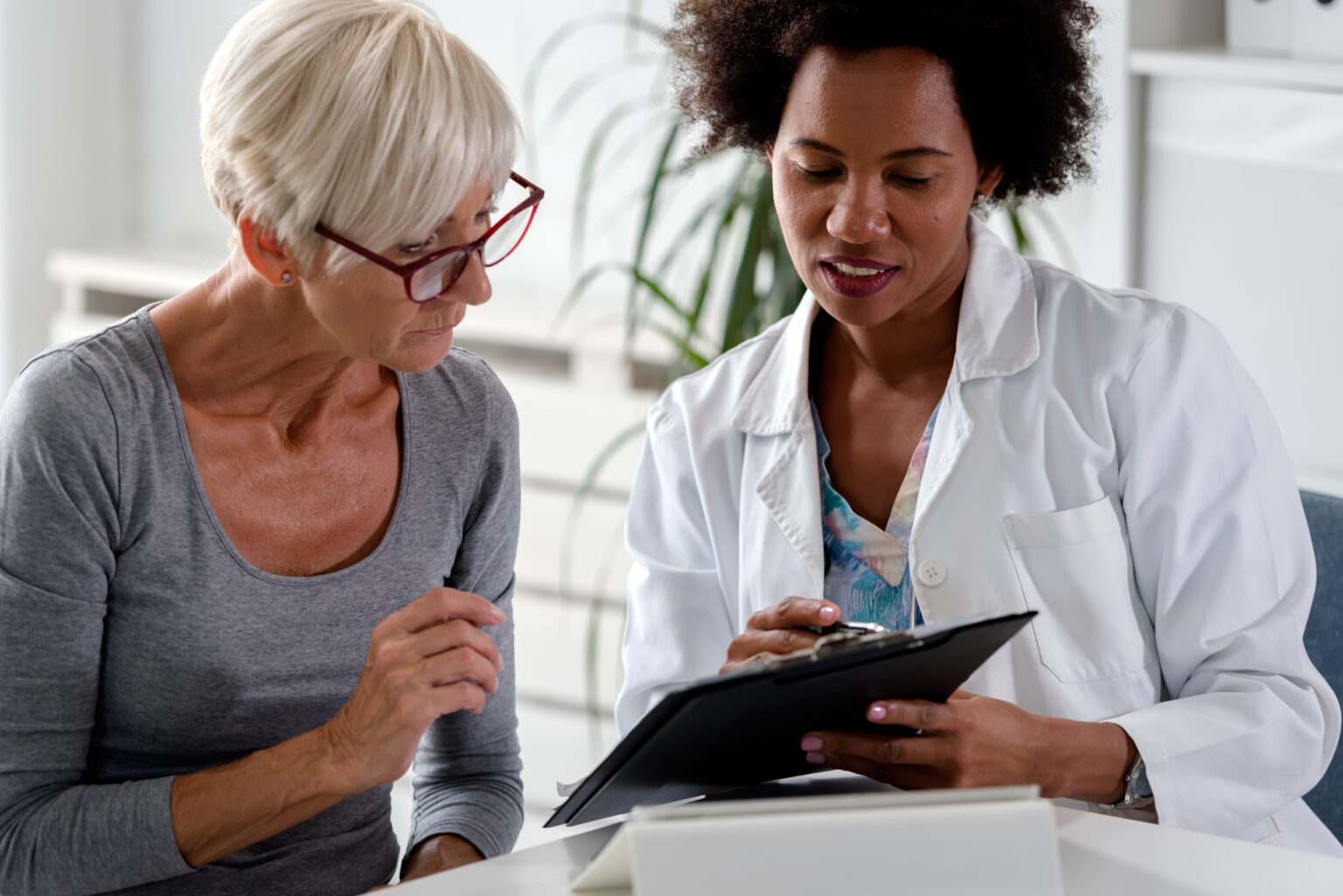 A female doctor sits at her desk and chats to an elderly female