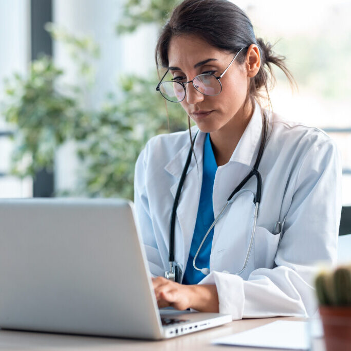 Shot of serious female doctor working with her laptop in the consultation.